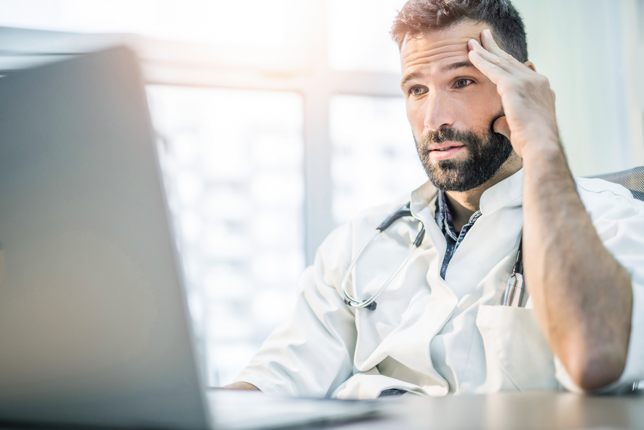 Worried and tired mid adult male doctor reading medical results on his laptop.