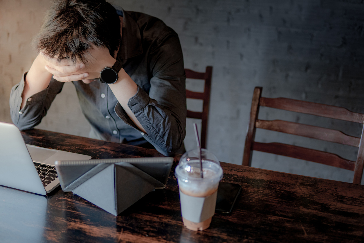 Overworked Asian businessman or male entrepreneur feeling stressed and frustrated while working with laptop computer and digital tablet in the cafe. Tired and headache from work hard or failure.